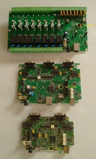 Three controller boards photographed from above, each with a yellow circle and arrow marking the pair of pins used for the erase procedure: the Dragonfly relay board at the top, the Platypus with three DB9 ports in the middle, and the Armadillo with two DB9 ports at the bottom.