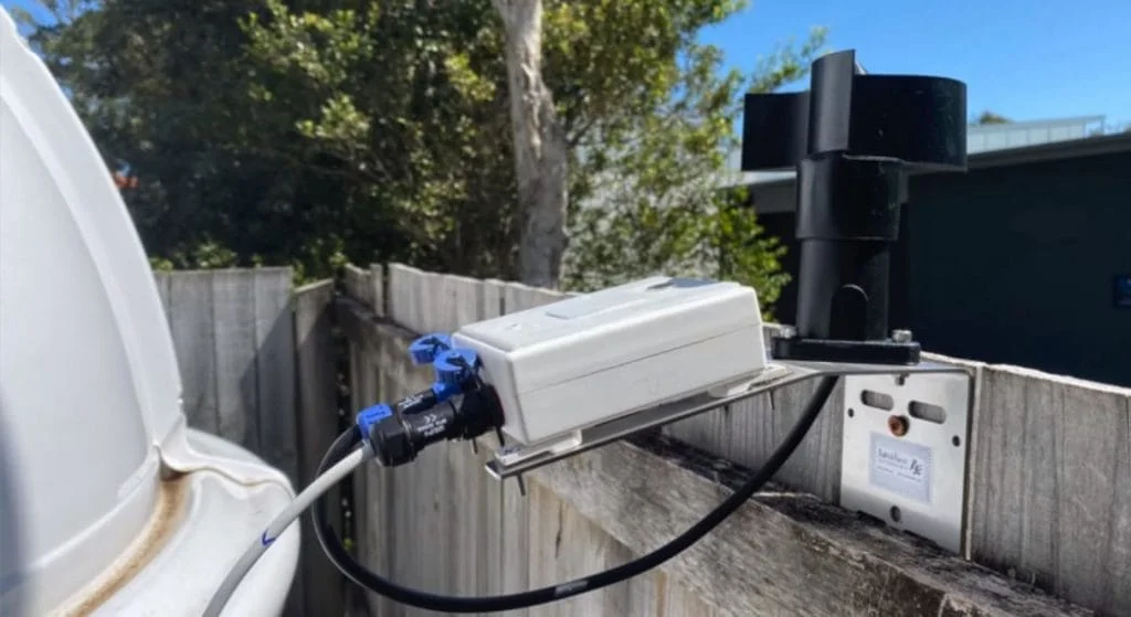 A CloudWatcher with anemometer mounted on a fence, watching the sky next to an observatory