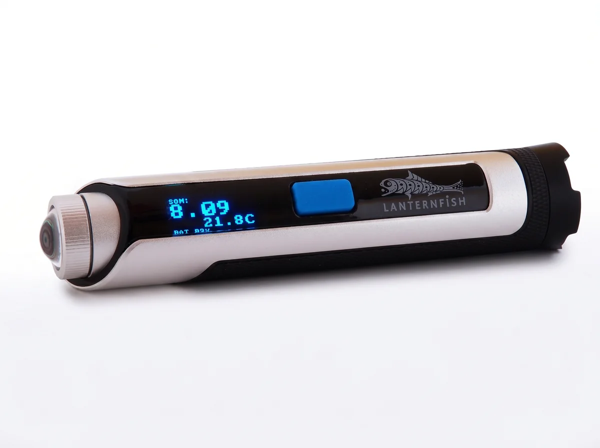 Lanternfish held horizontally, its OLED display reading SQM 8.09, 21.8C and the battery level, with the sensor dome at the left end