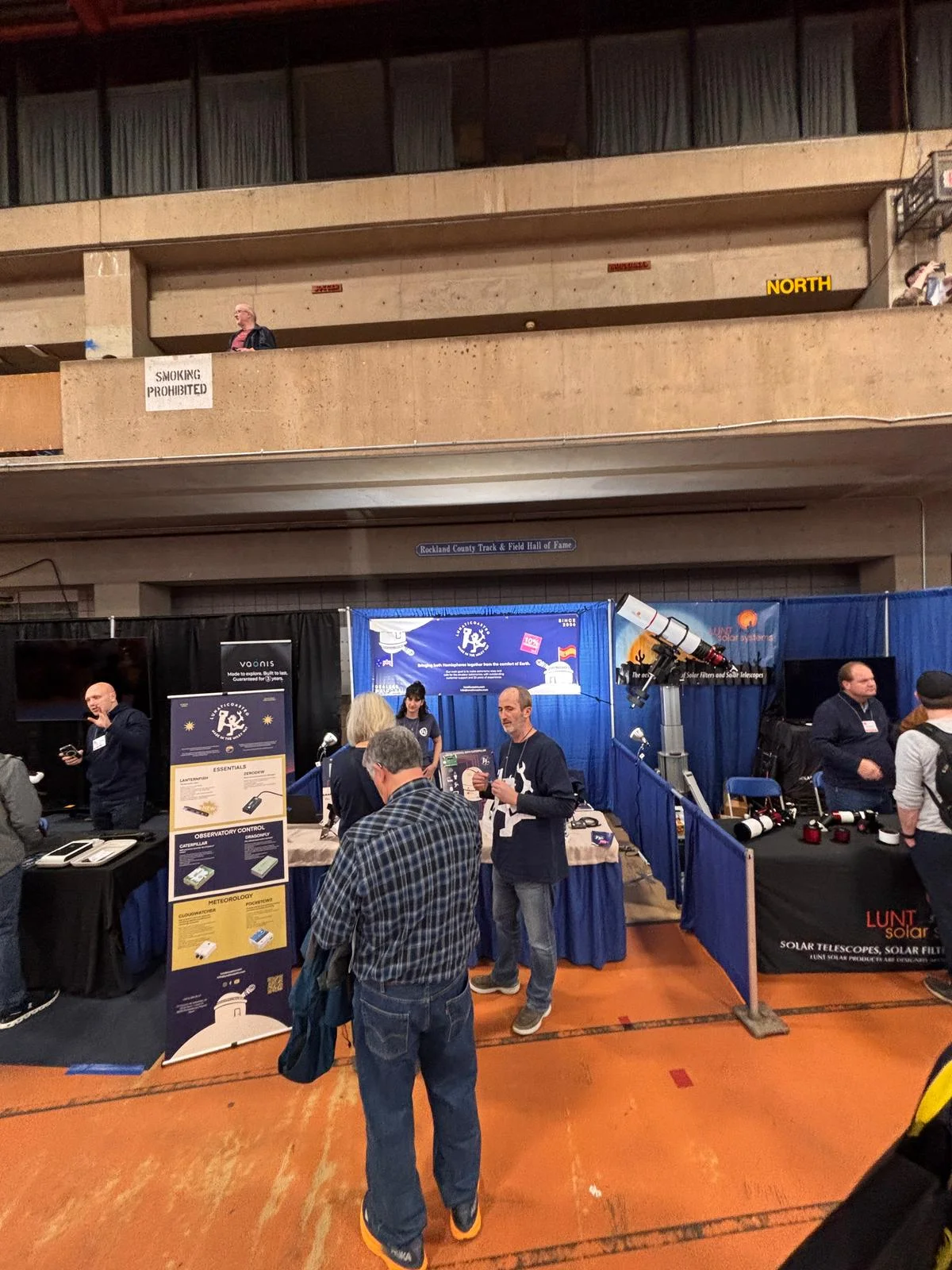 Visitors at the Lunaticoastro stand at NEAF 2025, with the roll-up product poster and the Lunt Solar Systems stand alongside