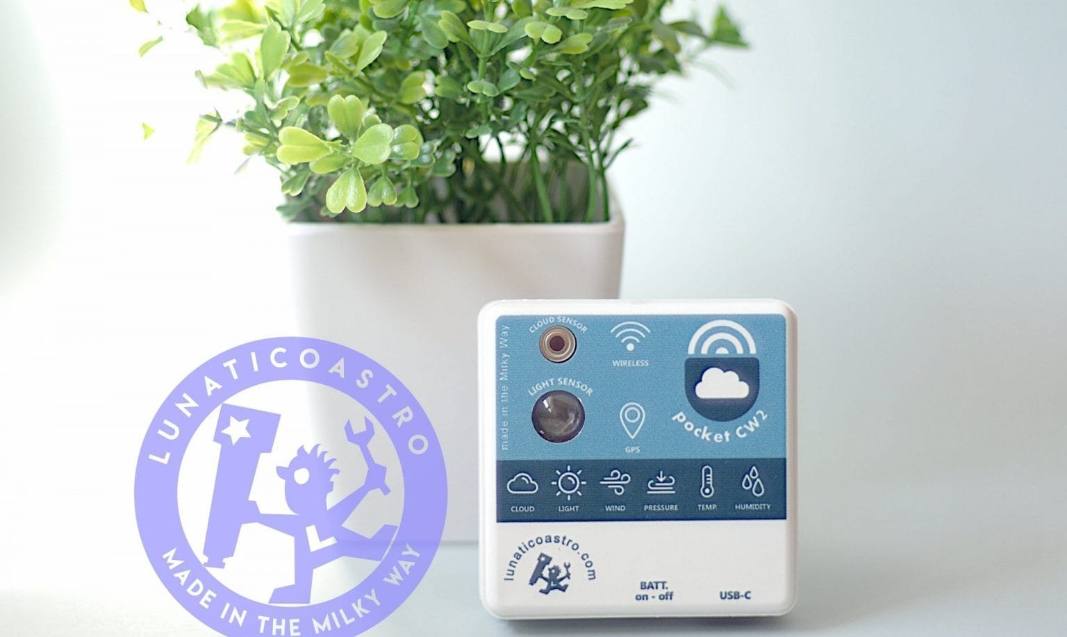 The pocketCW2 standing on a desk in front of a small plant pot, showing its top face with the cloud and light sensors