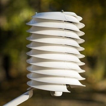 A white louvred radiation shield mounted on a pole: stacked plates let air circulate while keeping direct sunlight off the sensor inside