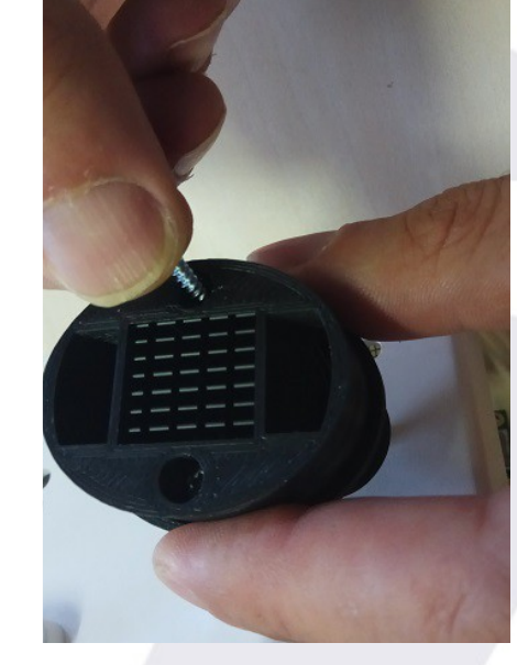 Screw being introduced into one of the round holes of the sensor cover